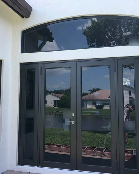 Bronze-frame impact French doors with glass sidelites under an arched transom, reflecting a lake