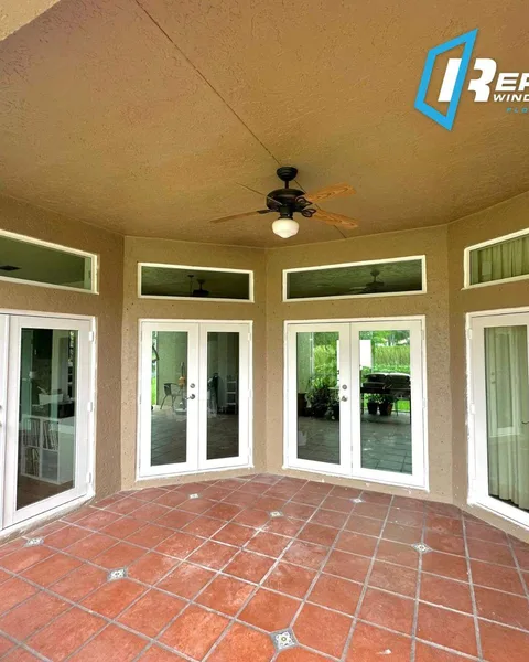 Four pairs of white impact French doors with transom windows above, around a tiled covered patio