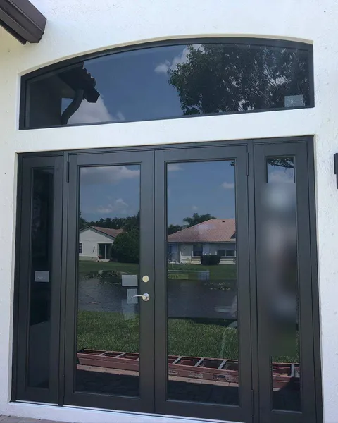 Bronze-frame double French impact doors with sidelites under an arched transom on a white house