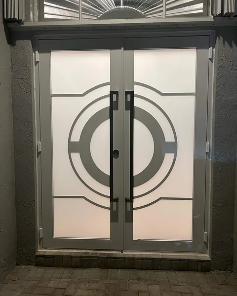 Gray double impact entry doors with frosted glass and a circle design, lit at dusk