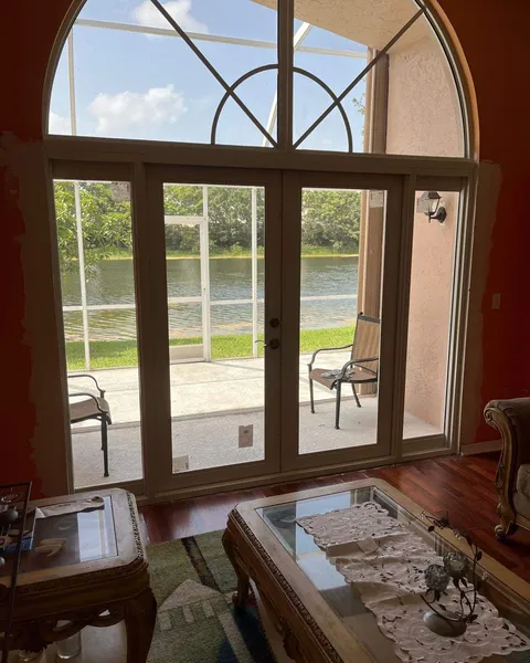 Inside view of white double French impact doors with sidelites and an arched transom, opening to a screened patio and a lake