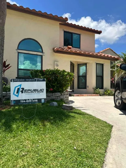 Two-story tile-roof home with bronze-frame impact windows, including arched windows, and a Republic yard sign