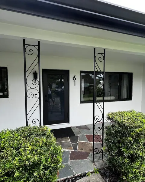 Black-frame horizontal roller impact windows beside the front door of a white house in Oakland Park