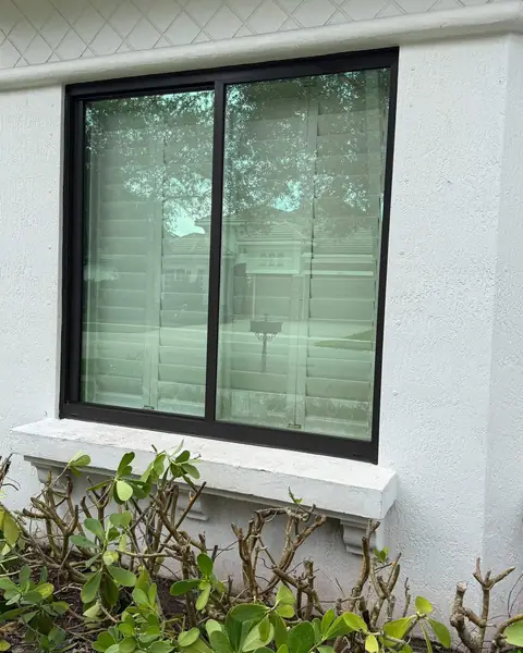 Black-frame horizontal roller impact window in a white wall above shrubs in Parkland