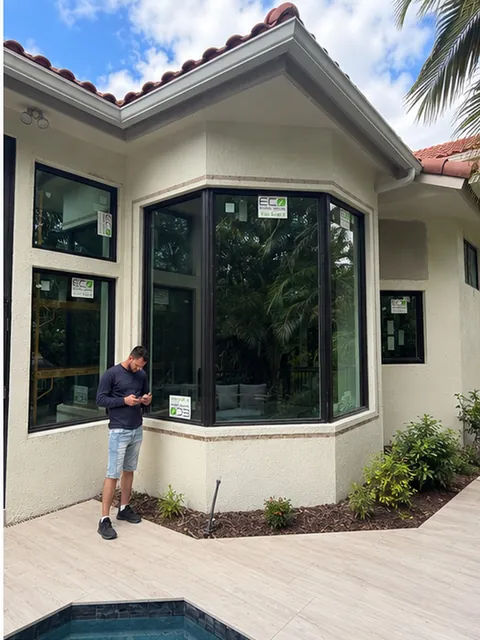 Man standing in front of a dark-frame impact bay window at the corner of a courtyard by a plunge pool