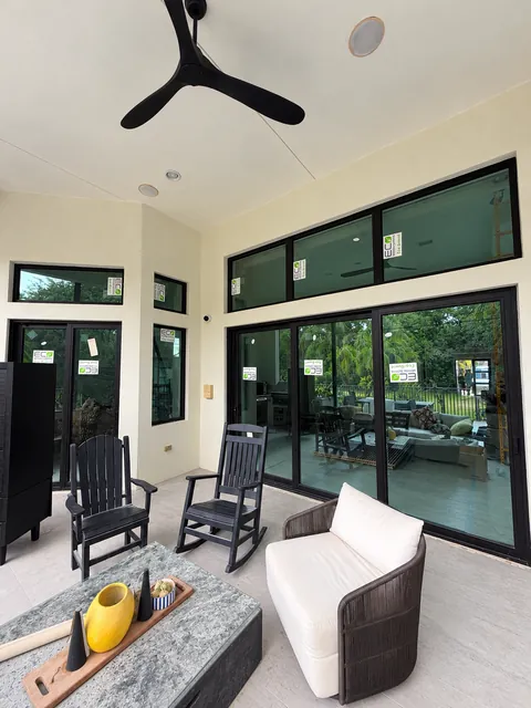 Covered patio with rocking chairs and a ceiling fan beside dark-frame impact sliding doors topped by transom windows