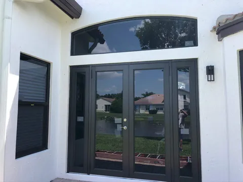 Dark-frame impact French doors with sidelites under an arched transom on a white stucco home