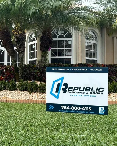 Arched white-frame impact windows behind a palm garden, with a Republic yard sign on the lawn