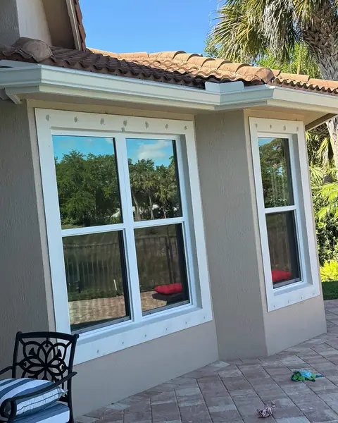 White single-hung impact windows on a tan stucco corner beside a patio in Palm Beach County