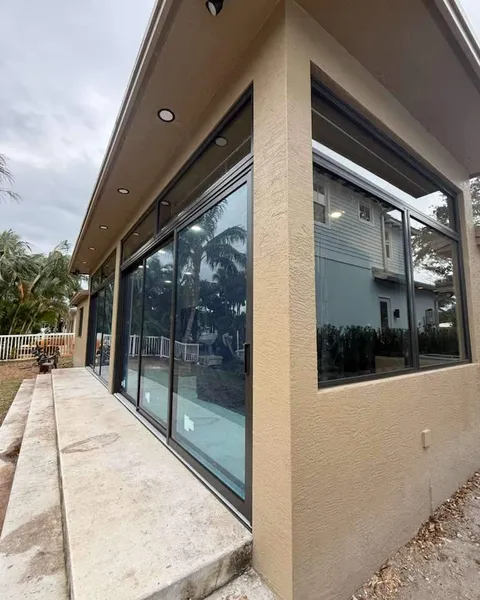 Corner of a tan house with black-frame impact sliding glass doors and transom windows above