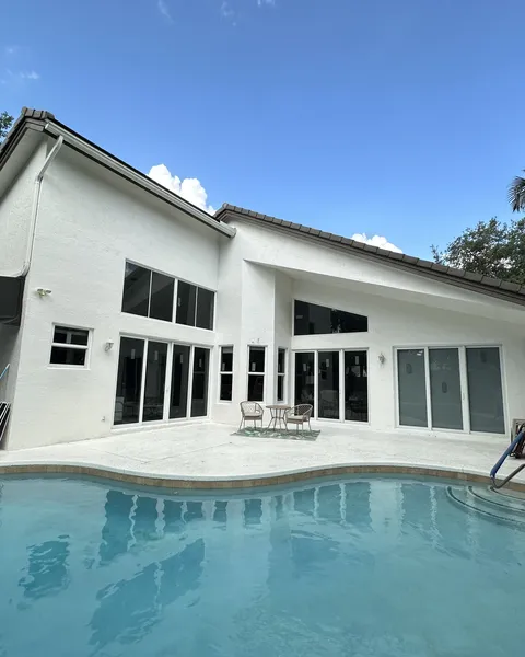 White two-story house with several impact sliding glass doors opening onto a pool deck