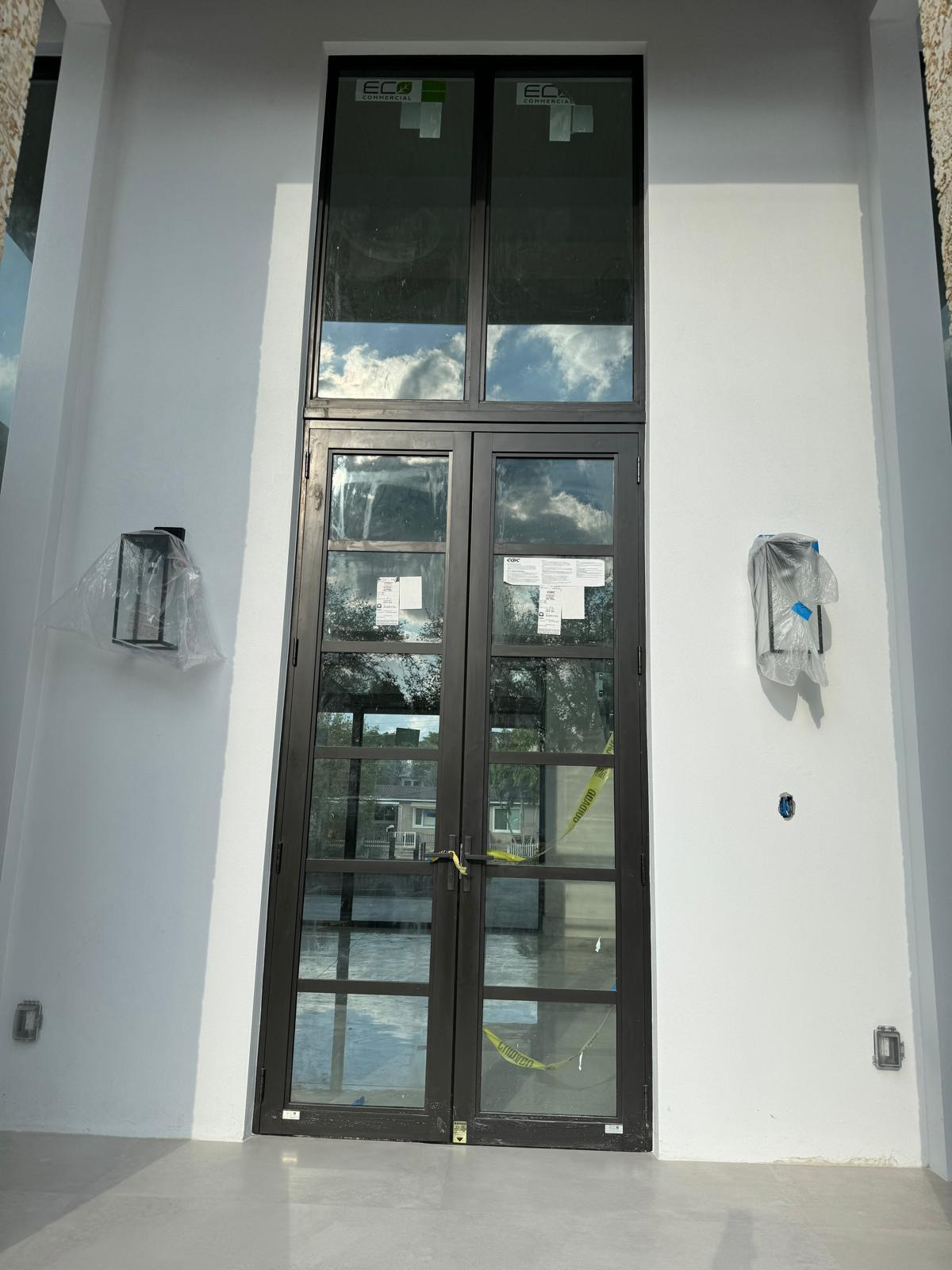 Monumental two-story bronze-frame double French impact entry door with divided-lite muntins and tall upper picture transom windows on a custom modern estate