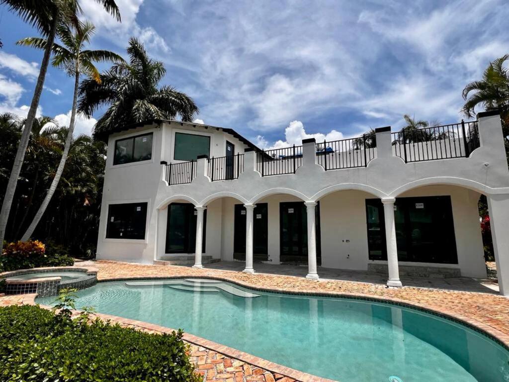 Two-story South Florida Mediterranean waterfront mansion outfitted with bronze-frame HVHZ impact sliding glass doors, outswing French doors, and upper-story picture windows overlooking a pool and colonnade
